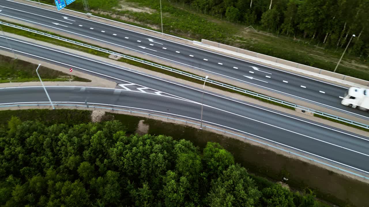 一条繁忙的高速公路的鸟瞰图，卡车和汽车被绿色植物包围，捕捉了一个运动中的交通网络视频素材