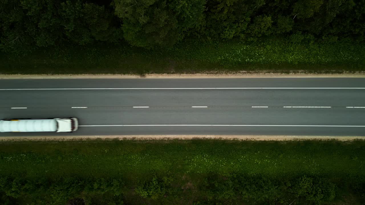 当一辆卡车在高速公路上穿过绿色的森林时，发现大自然的美丽，从鸟瞰图中捕捉到视频素材