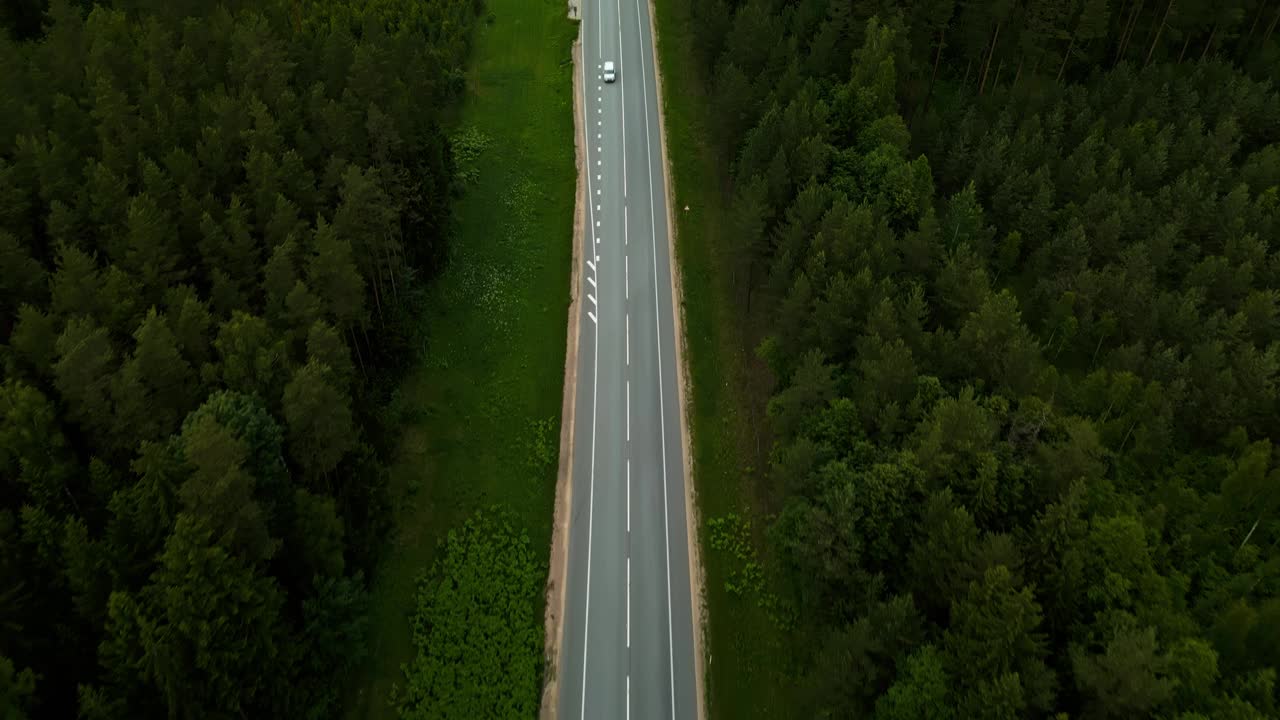 鸟瞰图，一辆汽车行驶在乡村公路上的森林里，周围是郁郁葱葱的绿色植物和宁静的景色视频素材