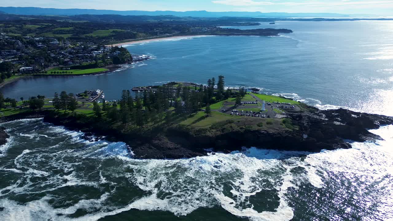 无人机空中景观的树木，主要城镇的海滩，海湾，岩石岬角，Kiama喷孔，悬崖和灯塔停车场南海岸澳大利亚旅游旅游视频素材