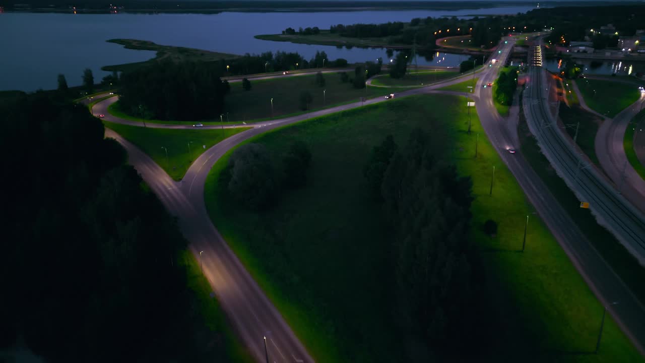 宁静的夜间鸟瞰图拍摄了一个高速公路交汇处，旁边是一个宁静的湖泊，被城市的灯光照亮视频素材