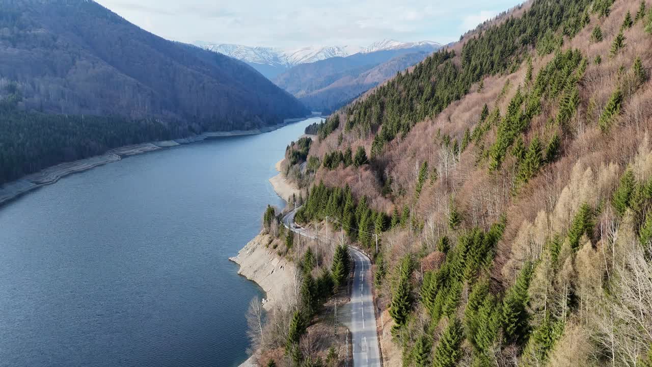 一条蜿蜒的道路沿着一个宁静的湖泊，周围是茂密的山脉视频素材