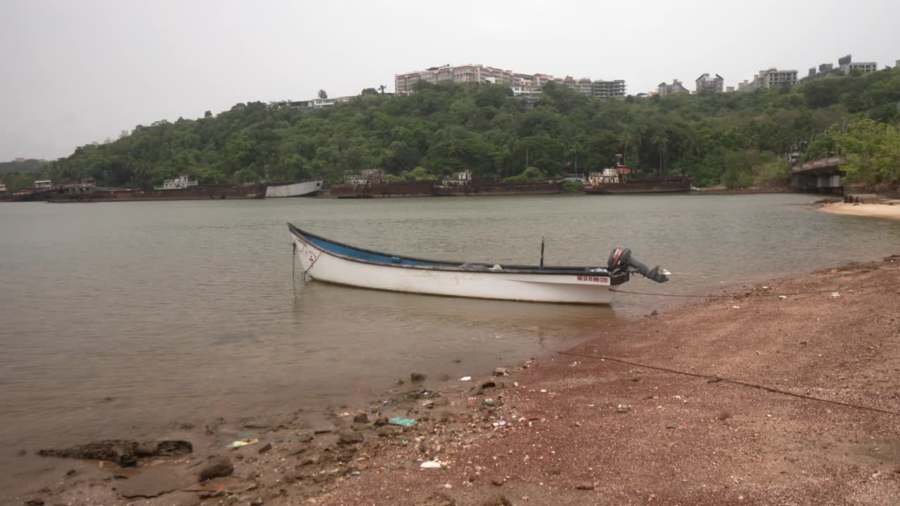 小船停泊在安静的海滩上，背景是森林覆盖的小山和建筑物视频素材