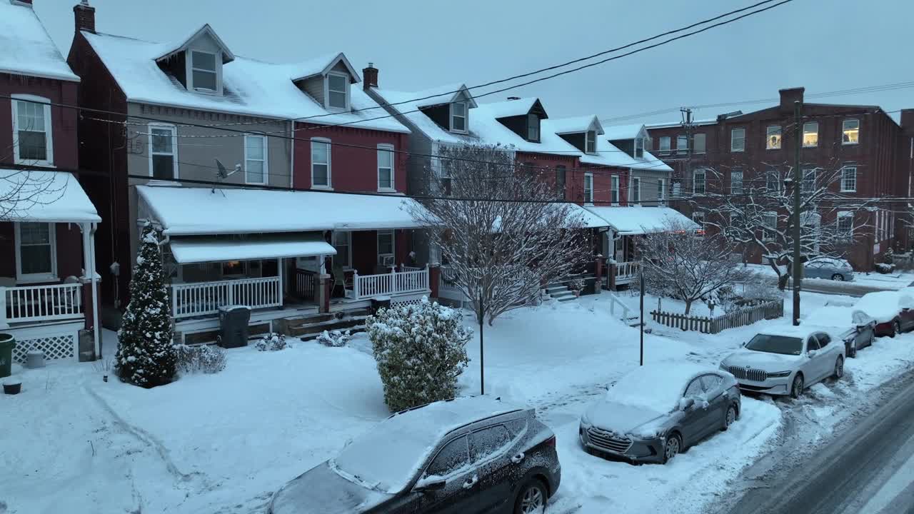 美国社区的圣诞冬日景象。黄昏时白雪覆盖的房屋和建筑物。白色的汽车和门廊的房子。郊区宁静迷人的社区。上升的空中广角镜头。视频素材