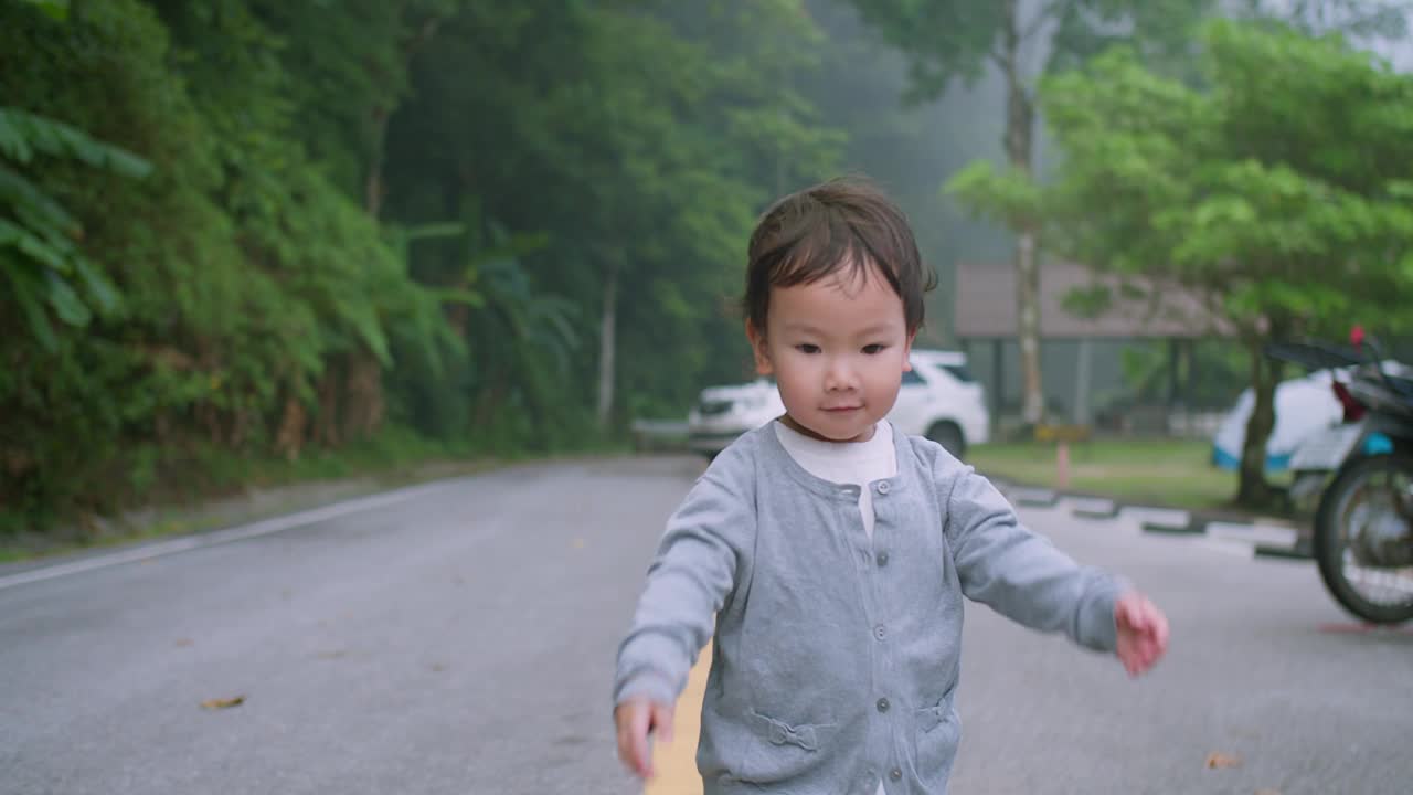 一个快乐的蹒跚学步的孩子带着灿烂的笑容，在公园里享受一天，背景是模糊的绿色植物。视频素材