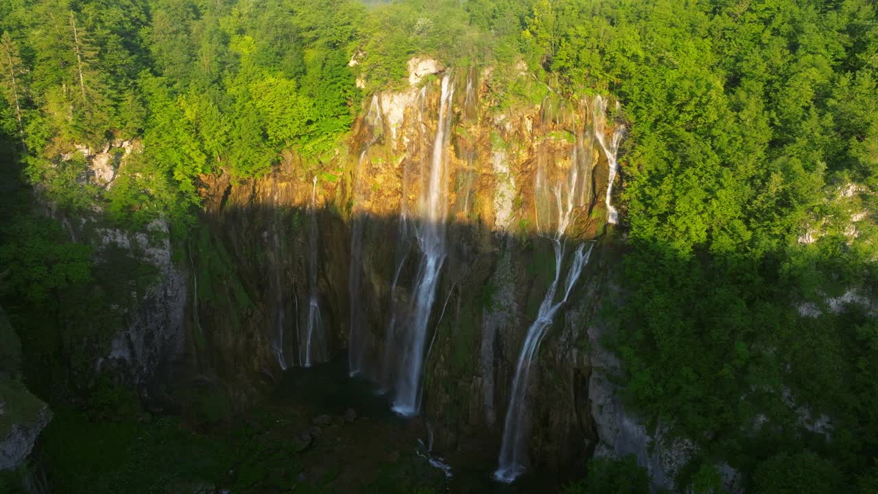 在克罗地亚的普利特维采湖国家公园，瀑布从陡峭的悬崖上与树叶一起流下。空中拍摄视频下载