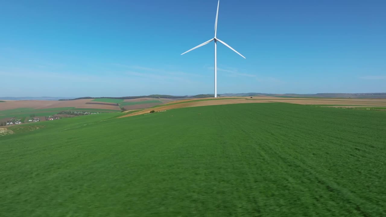 在晴朗的蓝天下，一个风力涡轮机矗立在广阔的绿色田野上视频下载