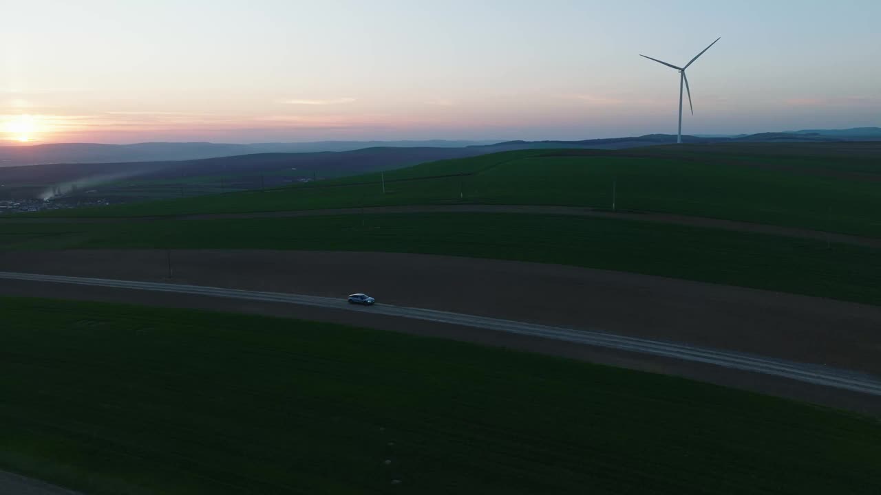 日落时分，一辆汽车行驶在乡村公路上，经过风力涡轮机视频下载