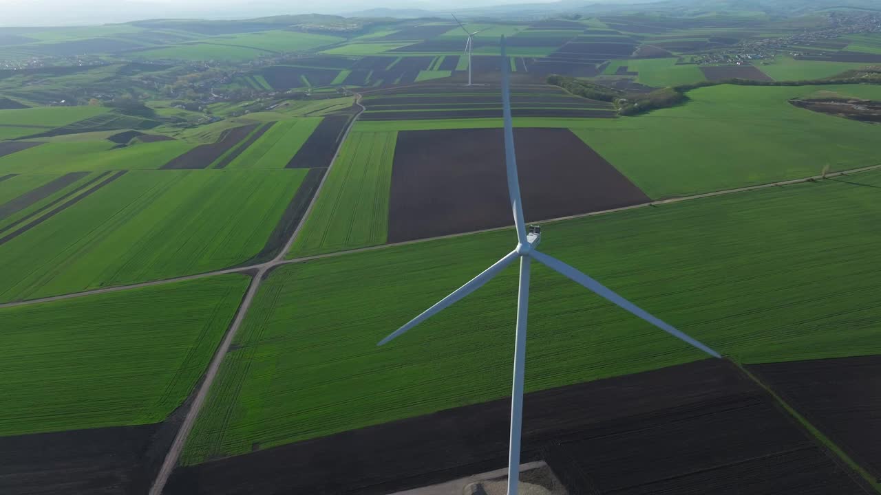 风力涡轮机在广阔的绿色和棕色田野上旋转，鸟瞰图视频下载