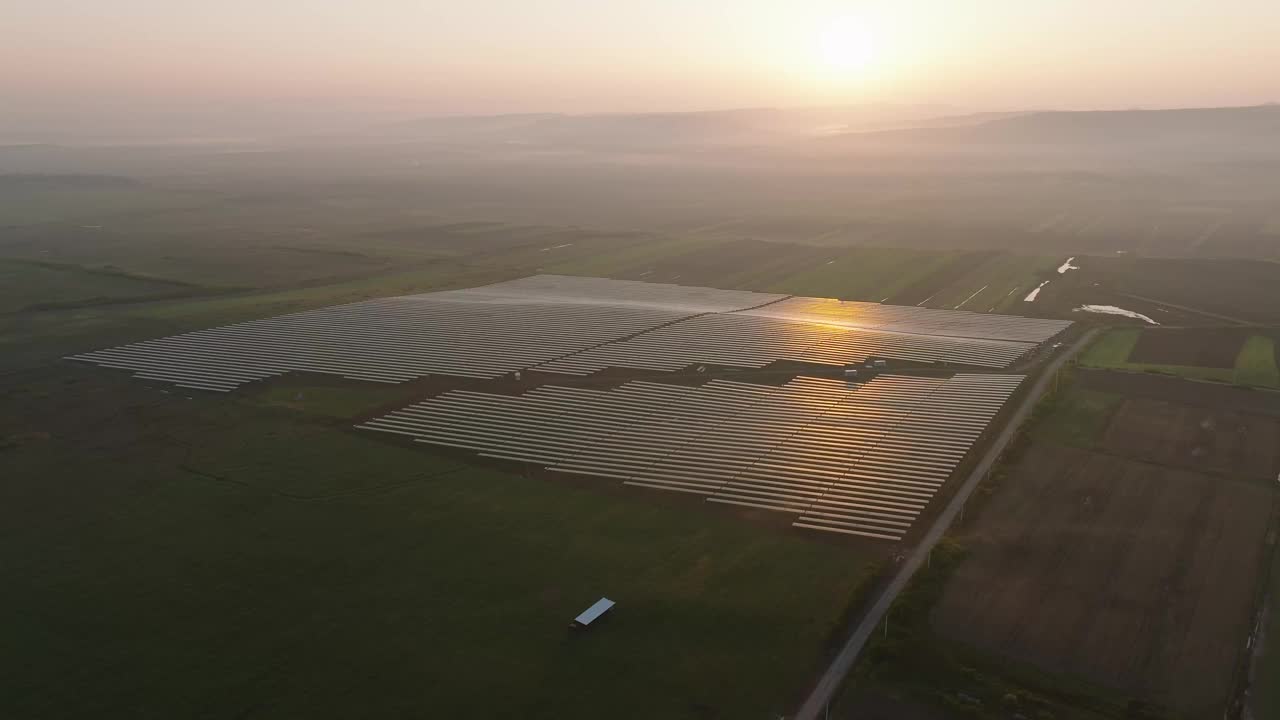 在雾蒙蒙的日出中，太阳能电池板在广阔的绿色田野上鸟瞰视频下载
