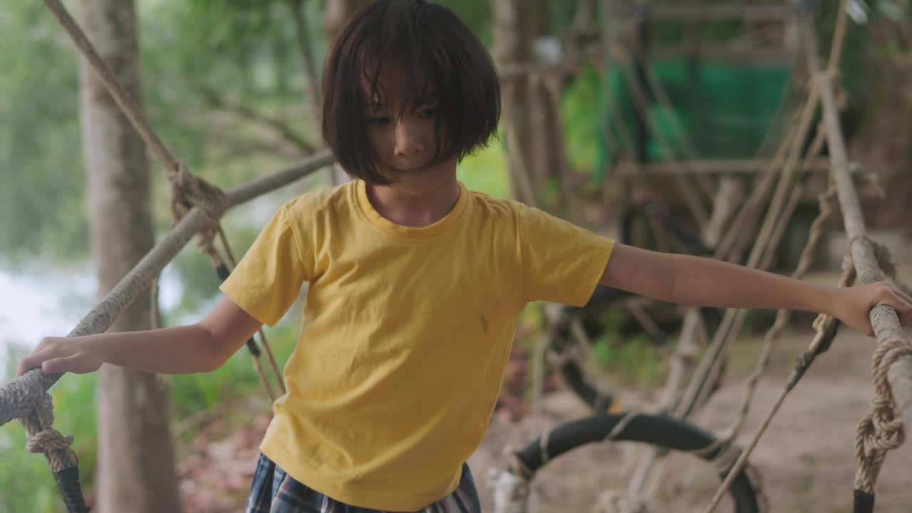 可爱的亚洲小女孩探索森林，带着快乐和天真在绳桥上航行。郁郁葱葱的绿色植物和宁静的景观捕捉了无忧无虑的童年和户外游戏的本质。视频素材