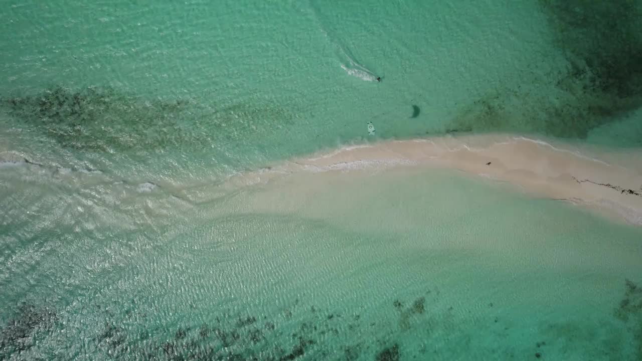 一个风筝冲浪者在沙滩附近的绿松石水面上滑翔，鸟瞰图视频素材