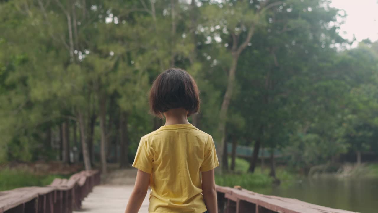 小女孩走在一座木桥上，背对着镜头，沉浸在大自然中，被森林包围，展现出童年的天真、探索和自由，和平与无忧无虑的冒险。视频素材