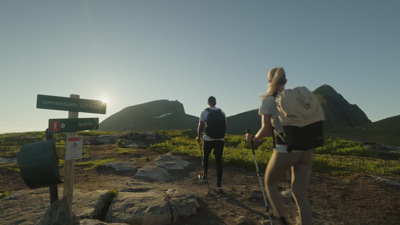 一对夫妇在午夜的阳光下在挪威的Senja徒步旅行，经过一个步道标志，用杆子视频素材