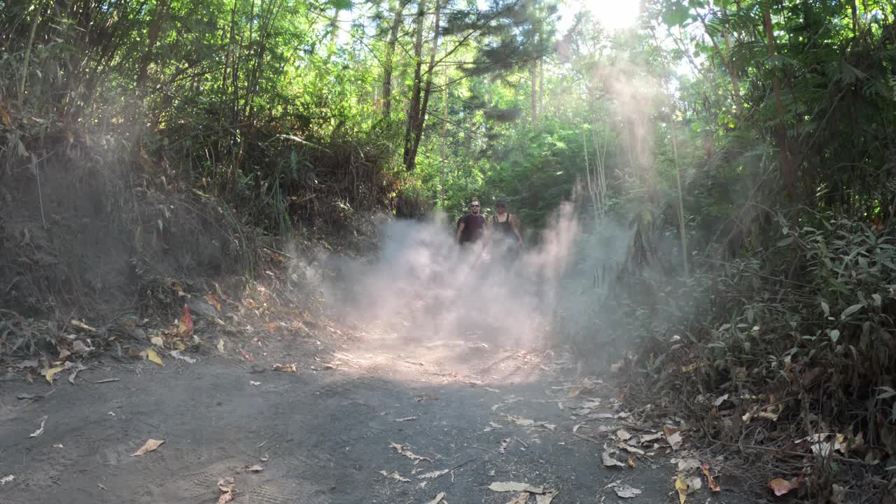 一对夫妇在印度尼西亚巴厘岛巴图尔山阳光普照的森林里尘土飞扬的小路上徒步旅行视频素材