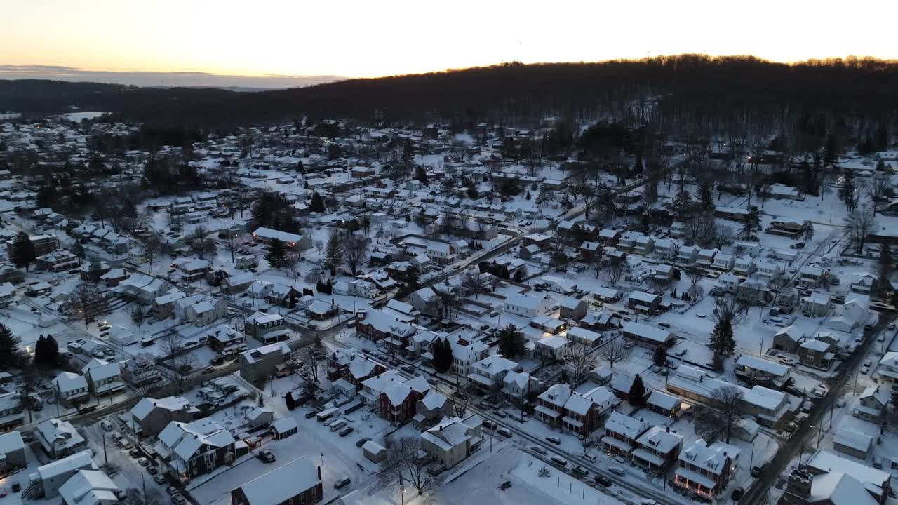 金色夕阳下的美国小镇村庄。积雪覆盖了房屋和建筑物。空中建立向后射击。视频素材