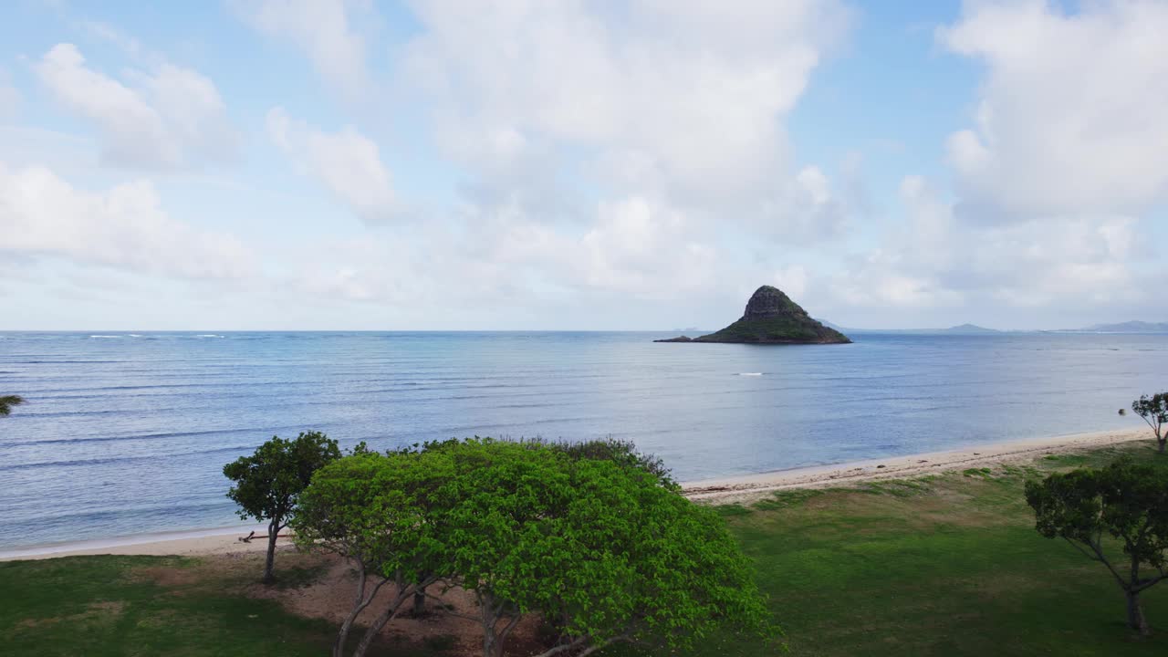 从瓦胡岛郁郁葱葱的绿色海滩公园俯瞰宁静的Mokoli'i岛，也被称为中国人的帽子。平静的大海和晴朗的天空创造了一幅宁静的景色。视频素材