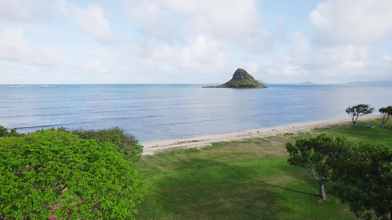 从瓦胡岛郁郁葱葱的绿色海滩公园，可以看到Mokoli'i岛的田园诗般的景色，也被称为中国人的帽子。平静的大海和晴朗的天空构成了一幅宁静的景象。视频素材