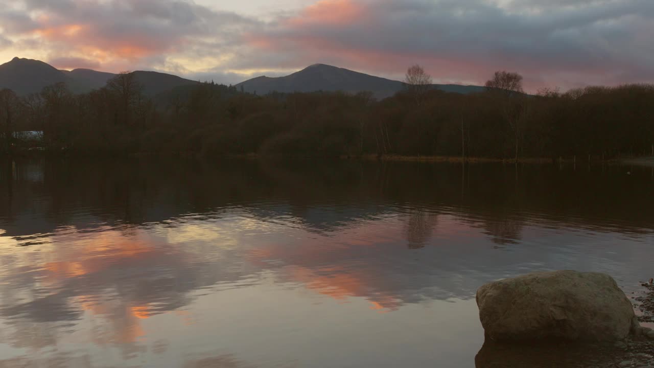 日落时拍摄的英格兰湖区宁静的夜晚。天空的鲜艳色彩映照在平静的水面上。视频素材