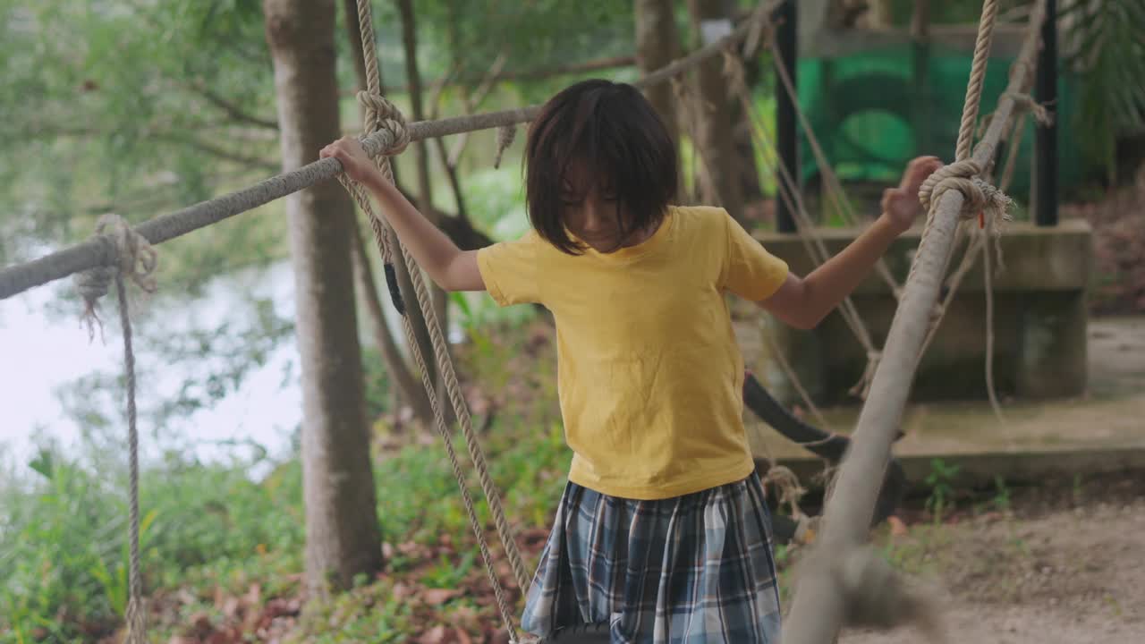 可爱的亚洲小女孩探索森林，带着快乐和天真在绳桥上航行。郁郁葱葱的绿色植物和宁静的景观捕捉了无忧无虑的童年和户外游戏的本质。视频素材