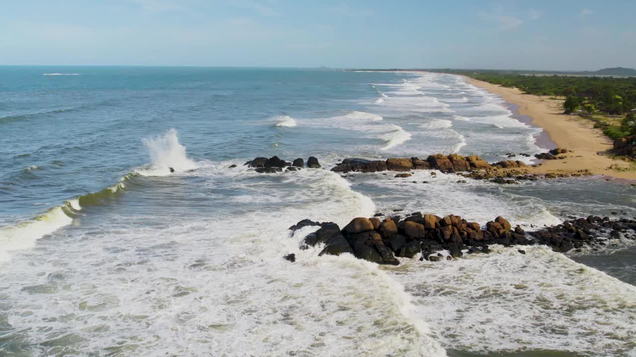 海浪冲击着岩石海岸，背景是沙滩，鸟瞰图视频素材