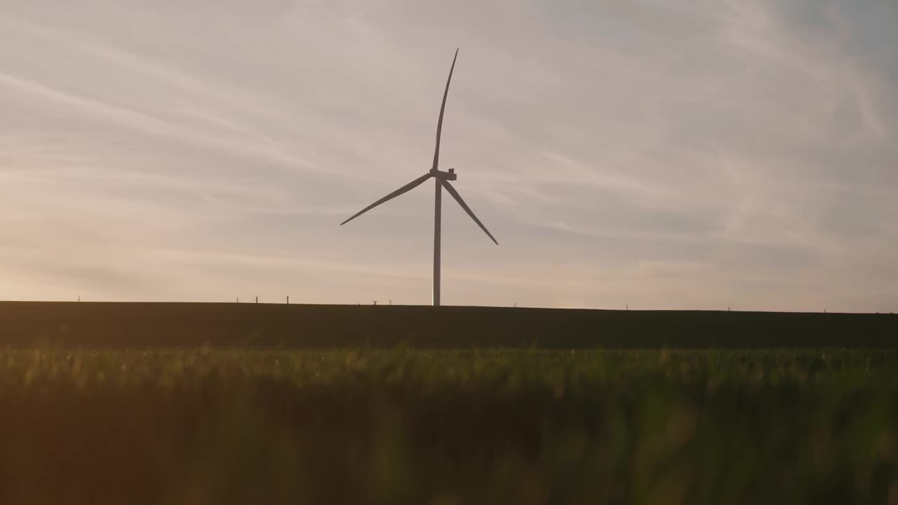 夕阳下绿色田野上的风力涡轮机，天空中充满了柔和的云视频素材