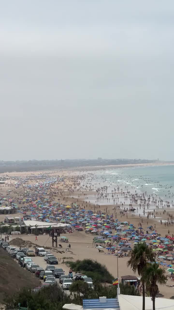 康尼尔德拉弗朗特拉海滩的全景，加的斯，在一个多云的日子里，一群游泳者和五颜六色的遮阳伞覆盖在沙滩上，而许多游客享受水视频下载