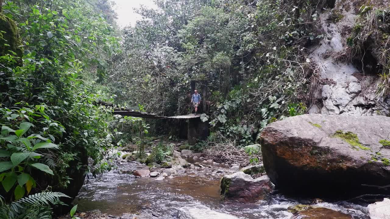 男徒步旅行者在粗糙的吊桥上穿过狭窄的丛林河视频素材