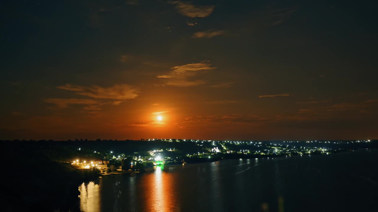 一个城市沿河的夜景，一轮明月照亮了风景，倒影在水中。视频素材