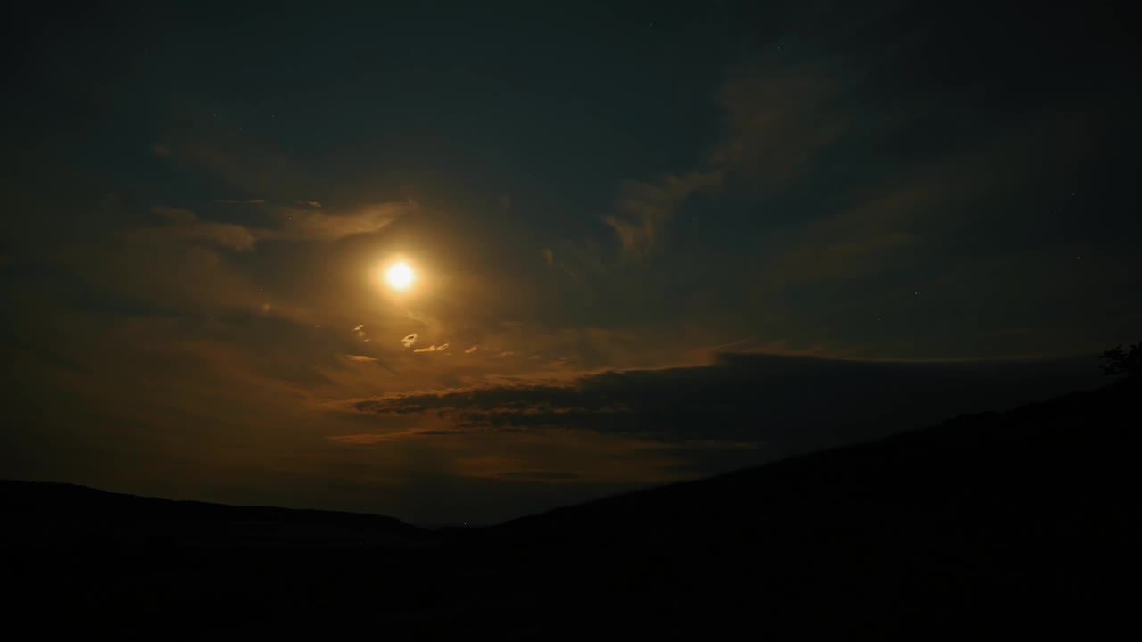 月亮照亮了宁静的夜空，背景是引人注目的云彩和轮廓分明的山丘。视频素材