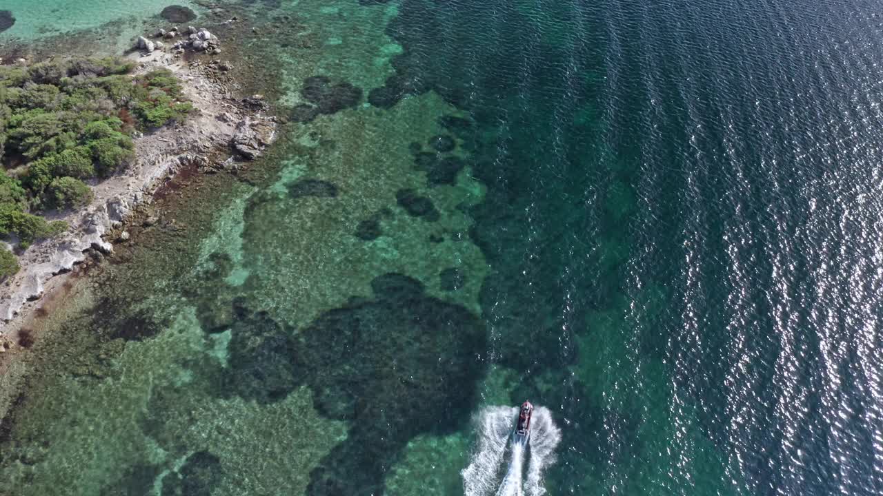 在撒丁岛的岩石海岸线附近，一艘快艇在清澈的碧绿海水上巡航，鸟瞰图视频素材