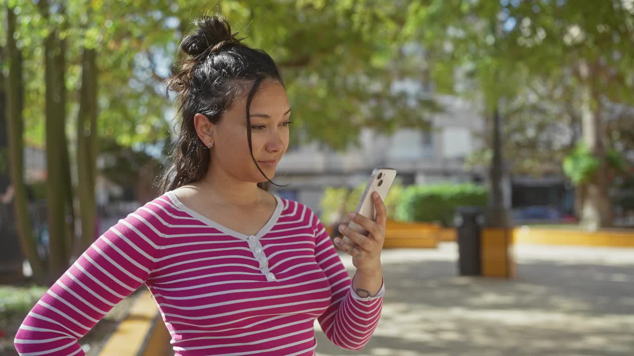 在绿树环绕的阳光明媚的公园里，一位兴高采烈的女士用智能手机自拍。视频素材