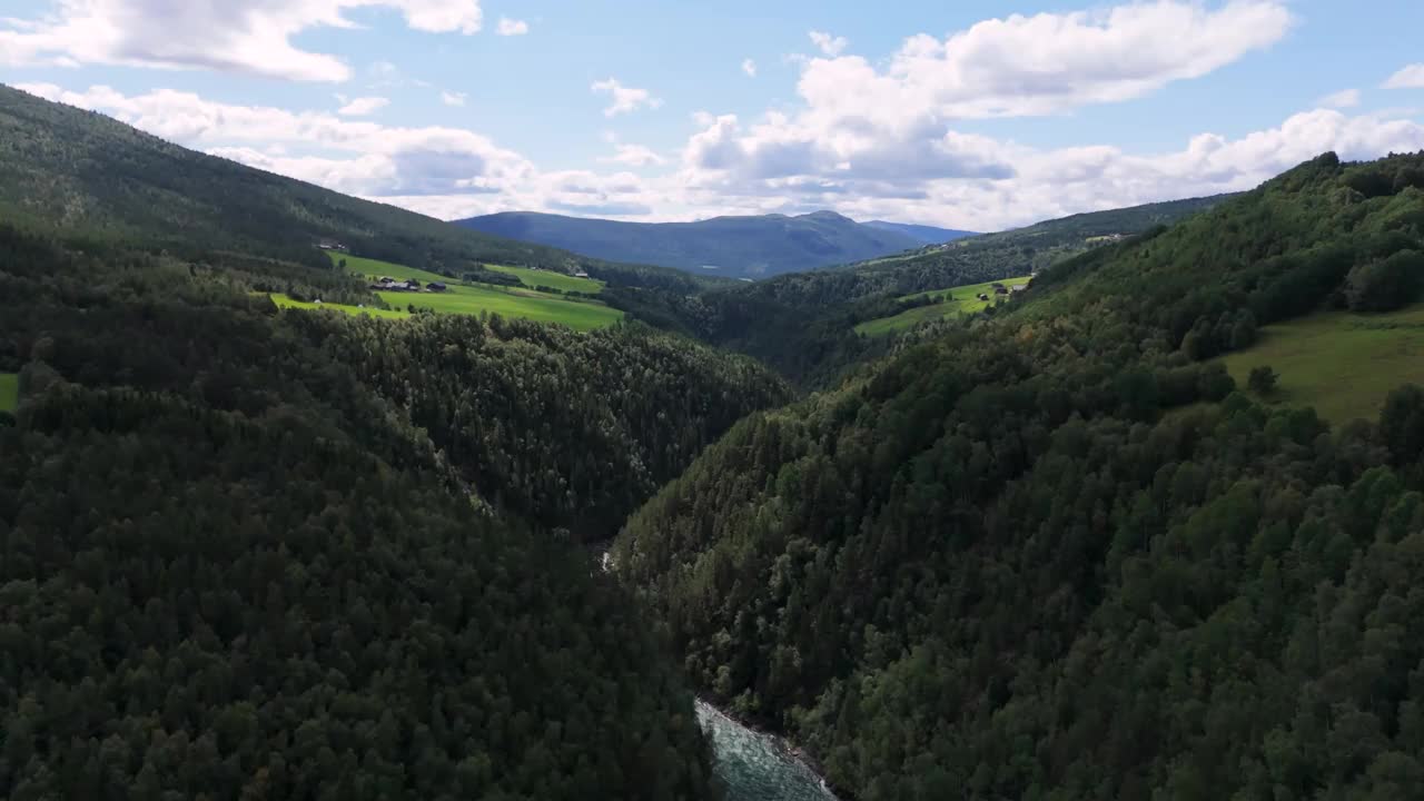 鸟瞰郁郁葱葱的森林山谷和蜿蜒的河流，周围是连绵起伏的丘陵和晴朗的天空。远景视频素材