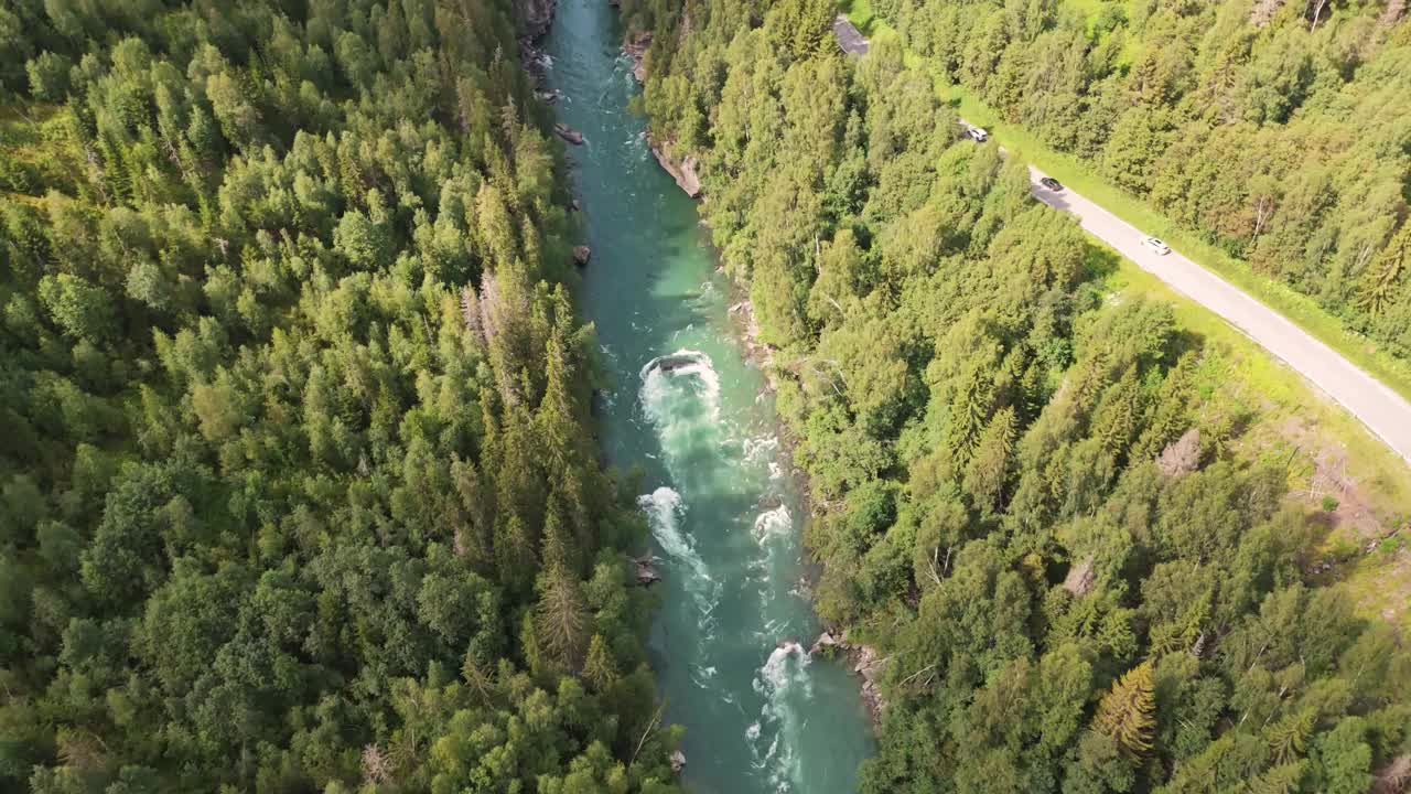 鸟瞰图，一条河流流经郁郁葱葱的森林山谷，乡村里有一条蜿蜒的道路。向前推，向上倾斜视频素材