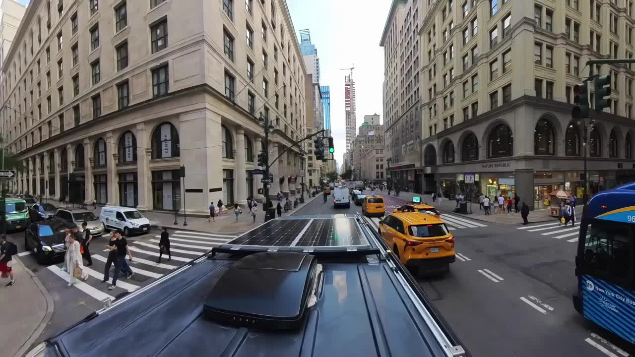 安装了太阳能电池板的露营车，汽车，校车和纽约警察局的警车行驶经过CVS药店，大通银行，自然共和国和帝国大厦在纽约市第五大道，新建筑正在建设的背景视频素材