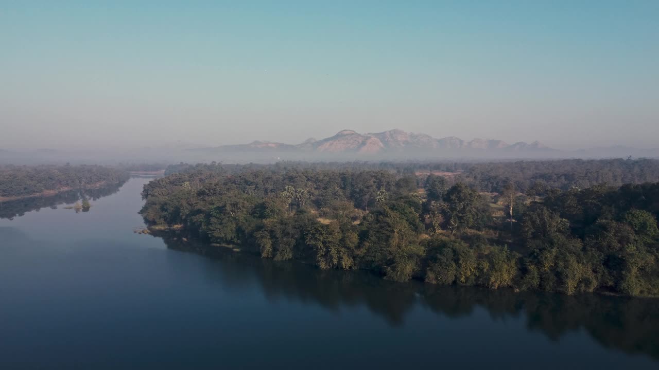 一条宁静的河流蜿蜒穿过郁郁葱葱的森林，远处的山脉在背景中，鸟瞰图视频素材