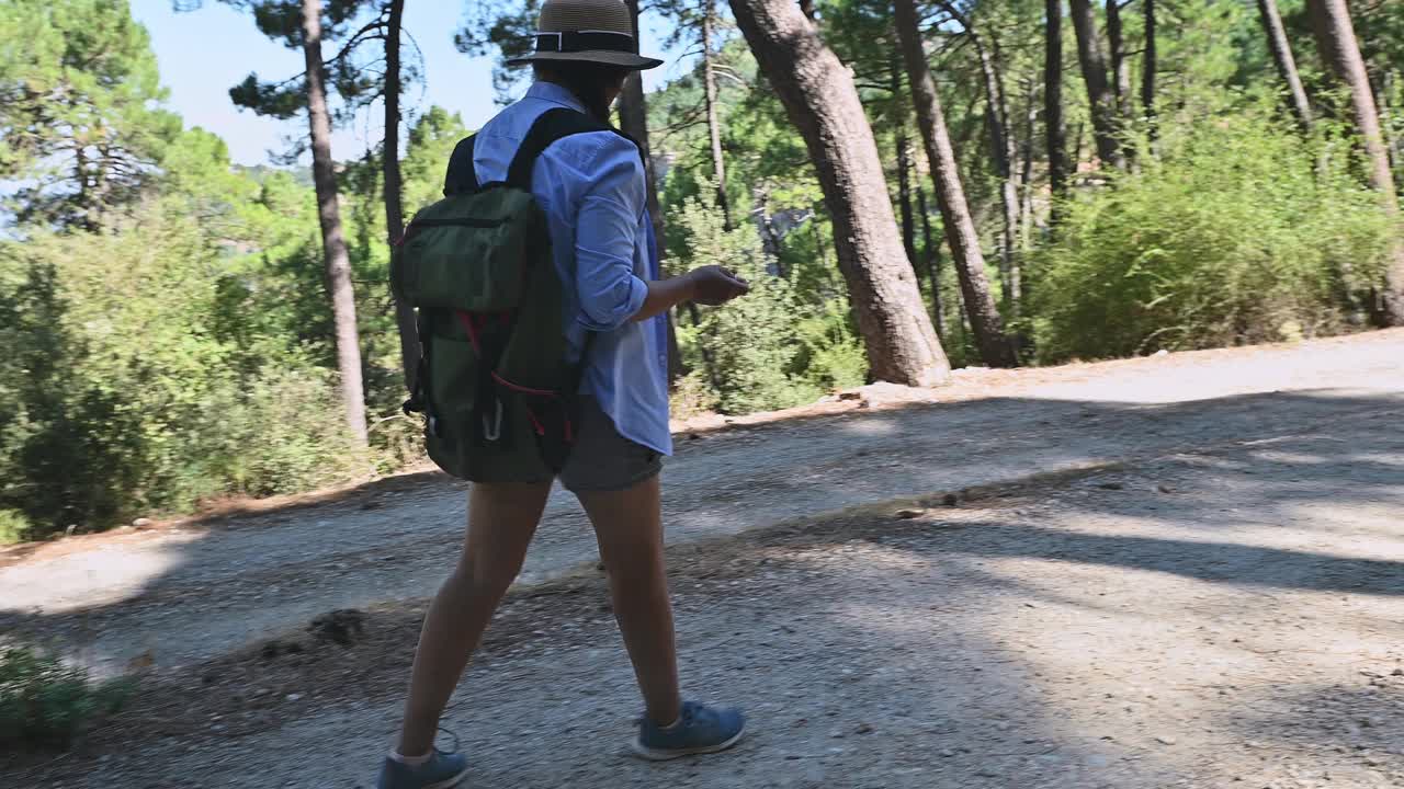 一名妇女穿着休闲装在森林小径上徒步旅行，在大自然中享受阳光明媚的一天，探索宁静的森林环境。视频素材