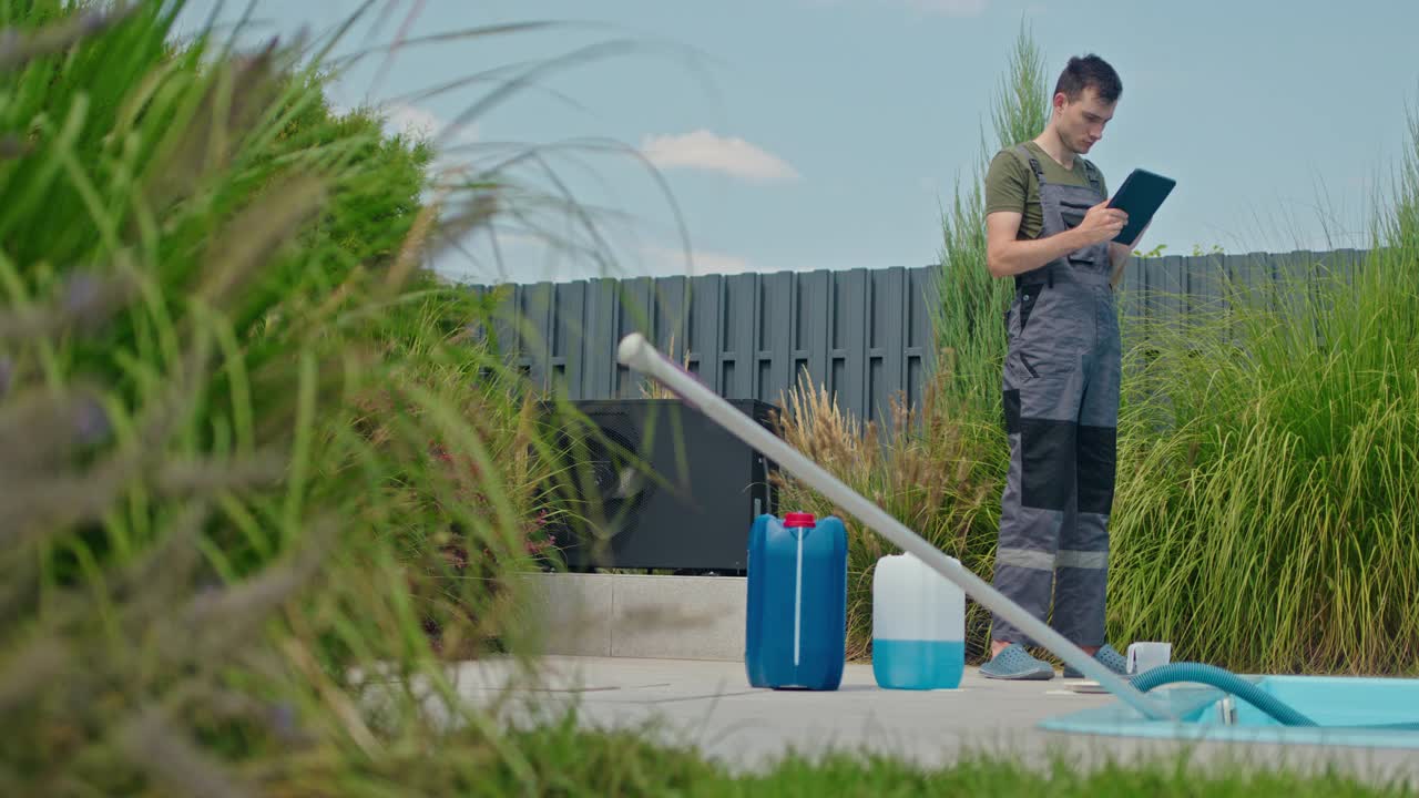 技术人员使用平板电脑进行日常泳池维护，旁边有化学容器和泳池真空。视频素材