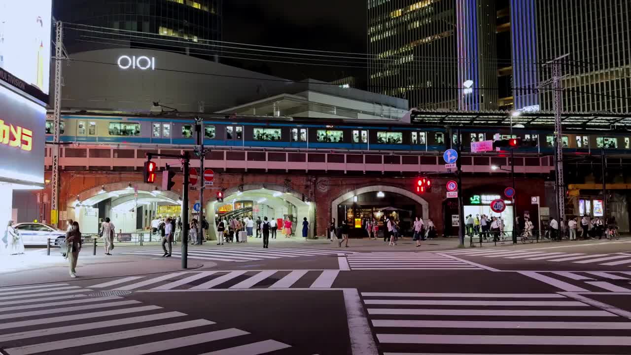 东京新桥的夜间城市街道，一列火车经过繁忙的人行横道视频素材