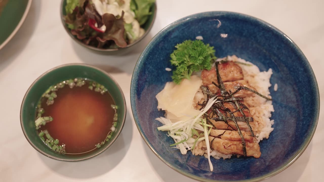 日式照烧鸡配米饭、味噌汤和沙拉摆放在餐桌上。视频素材画面1