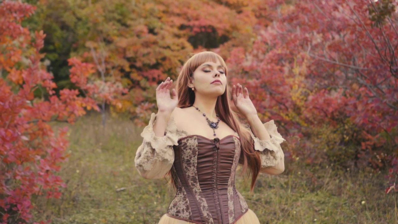 幻想女性时尚模特，手举姿势。复古风格的棕色复古裙，显得高贵。女孩精灵公主在秋天的橙红色树叶森林中，倾听自然的声音，树木的风声和鸟儿的歌唱。视频素材画面1