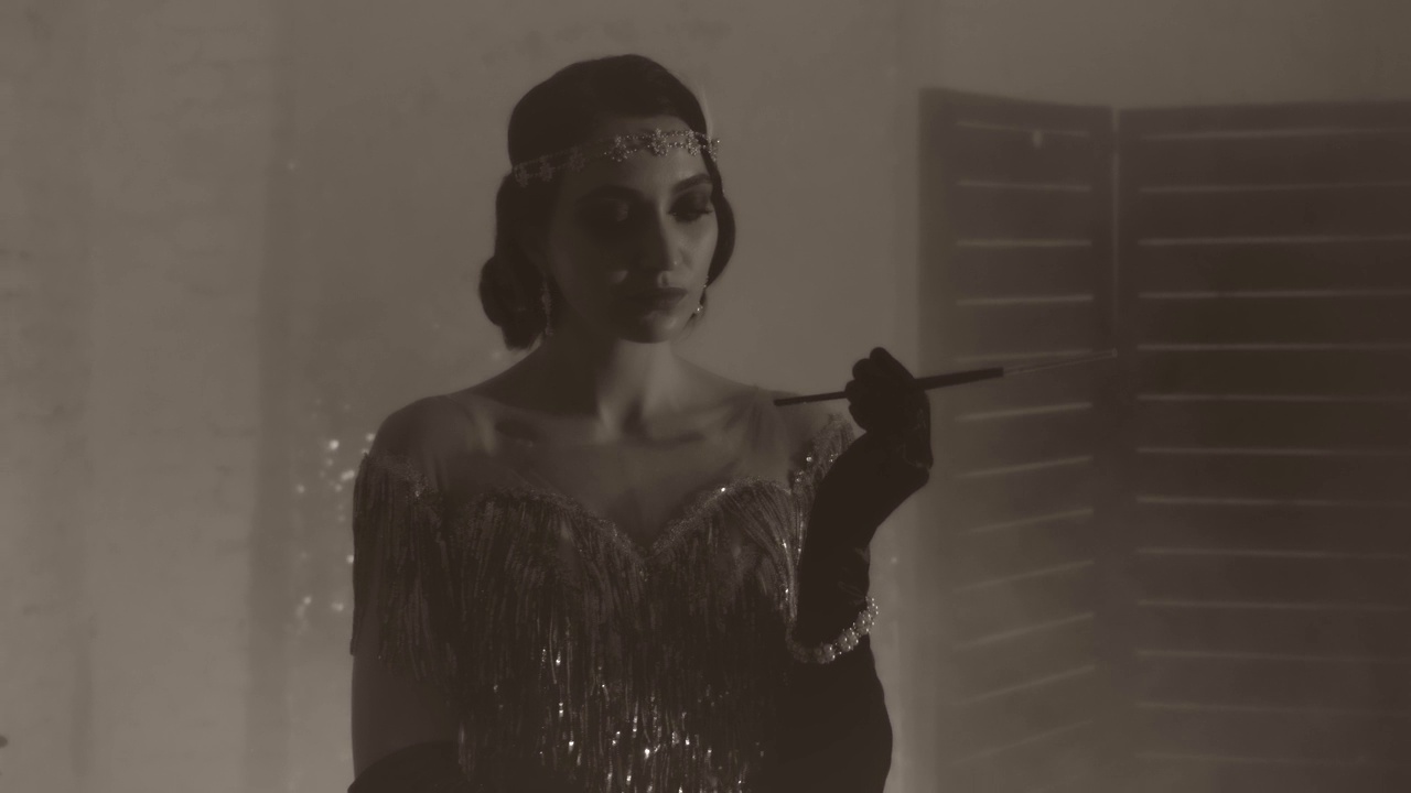 黑白噪音风格的视频。年轻美丽性感的复古女性手持长烟嘴和香烟，吸烟者。复古女孩模特。40年代时尚裙装。背景是经典房间。视频素材画面2