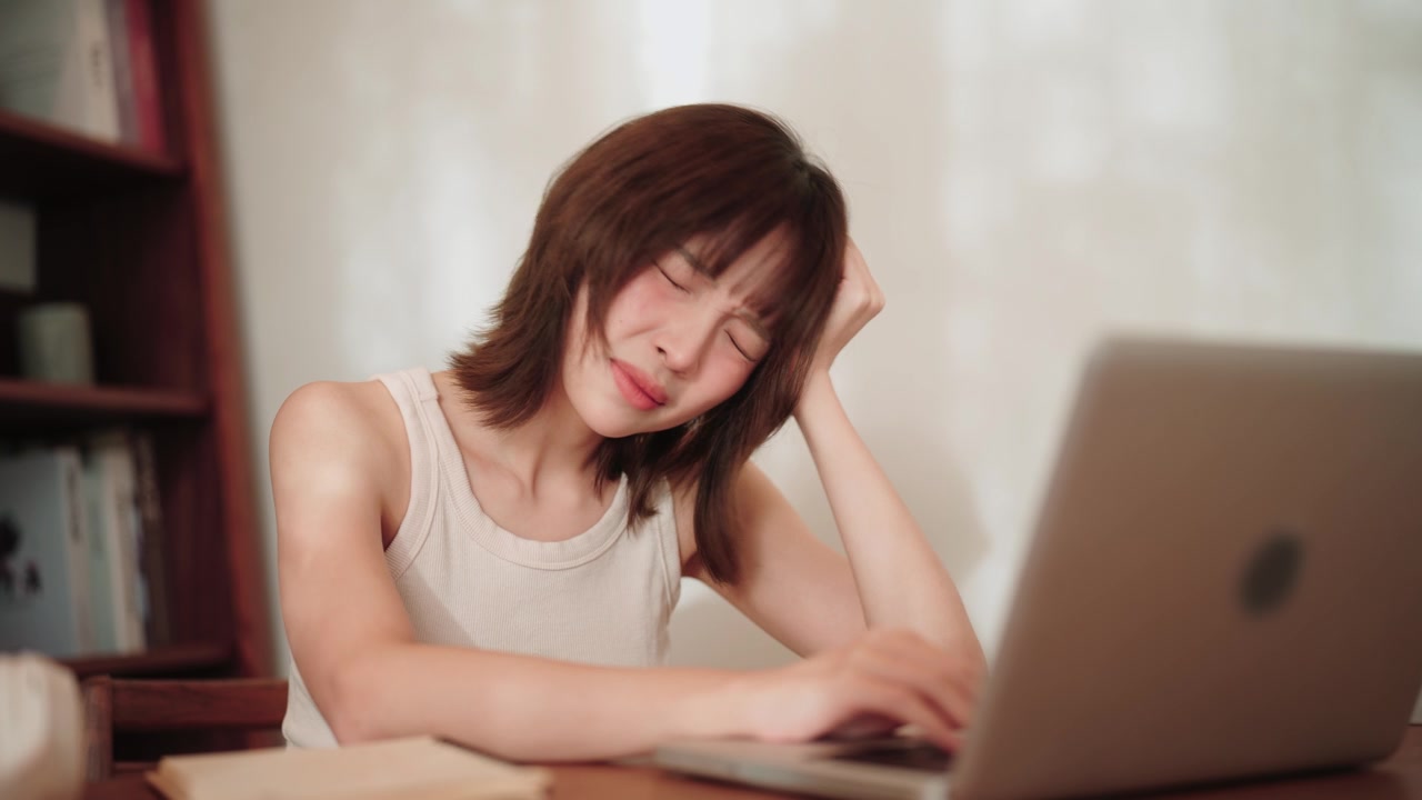 年轻的亚洲学生在专注于她的笔记本电脑任务时感到压力。视频素材画面2