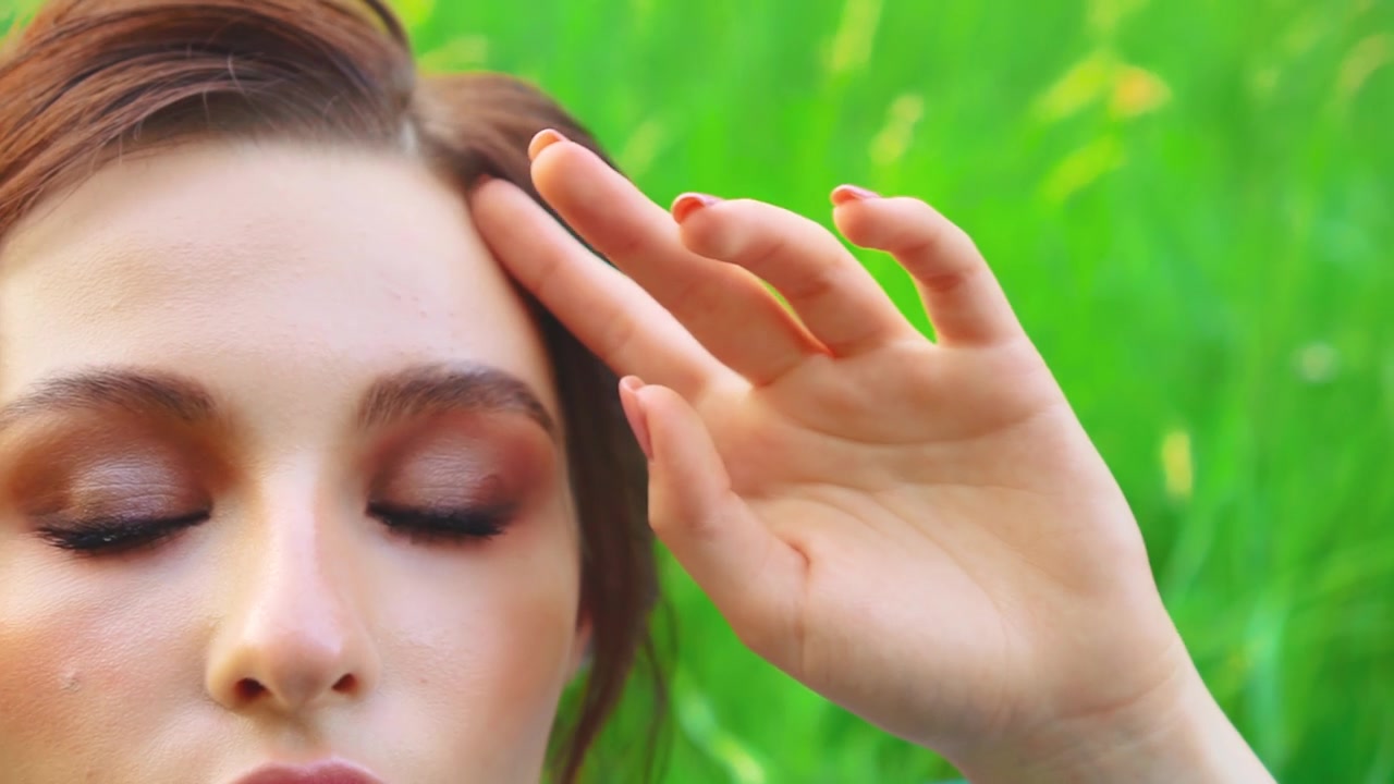 时尚模特摆拍，手触碰嘴唇，性感嘴唇肌肤。艺术肖像，成年女性，公主躺在绿草地上，身穿晚装复古蓝裙，精致妆容，仙女女王，漂亮脸庞。夏日自然视频素材画面4