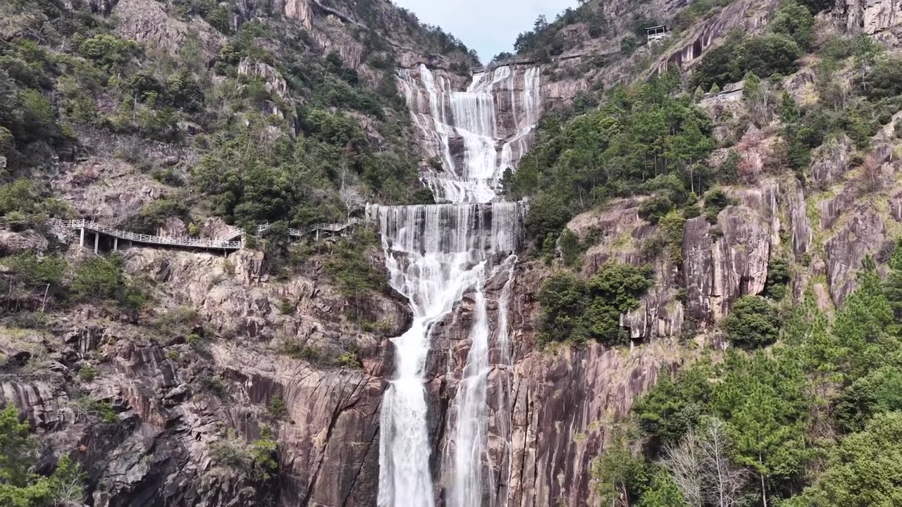航拍无人机视角，浙江天台山，多层瀑布沿着崎岖的岩石层层叠叠落下，陡峭的山坡，周围是充满活力的绿色植物，蜿蜒的木制步道供徒步旅行者行走。视频素材画面2
