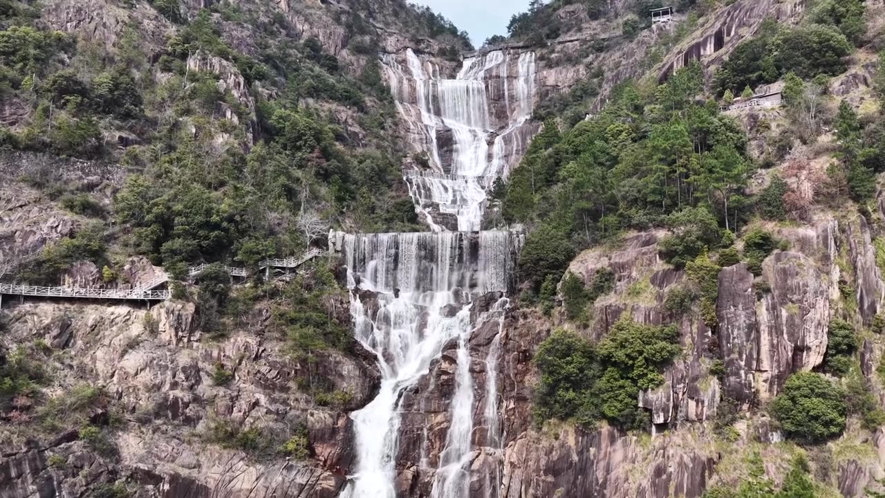航拍无人机视角，浙江天台山，多层瀑布沿着崎岖的岩石层层叠叠落下，陡峭的山坡，周围是充满活力的绿色植物，蜿蜒的木制步道供徒步旅行者行走。视频素材画面4