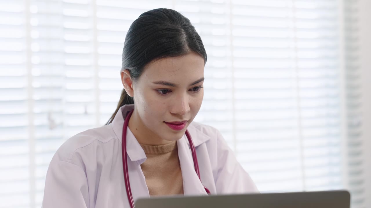 亚洲女医生在诊疗期间近距离查看笔记本电脑屏幕。面部表情显示出在专业医疗环境中注重细节和投入。视频素材画面1