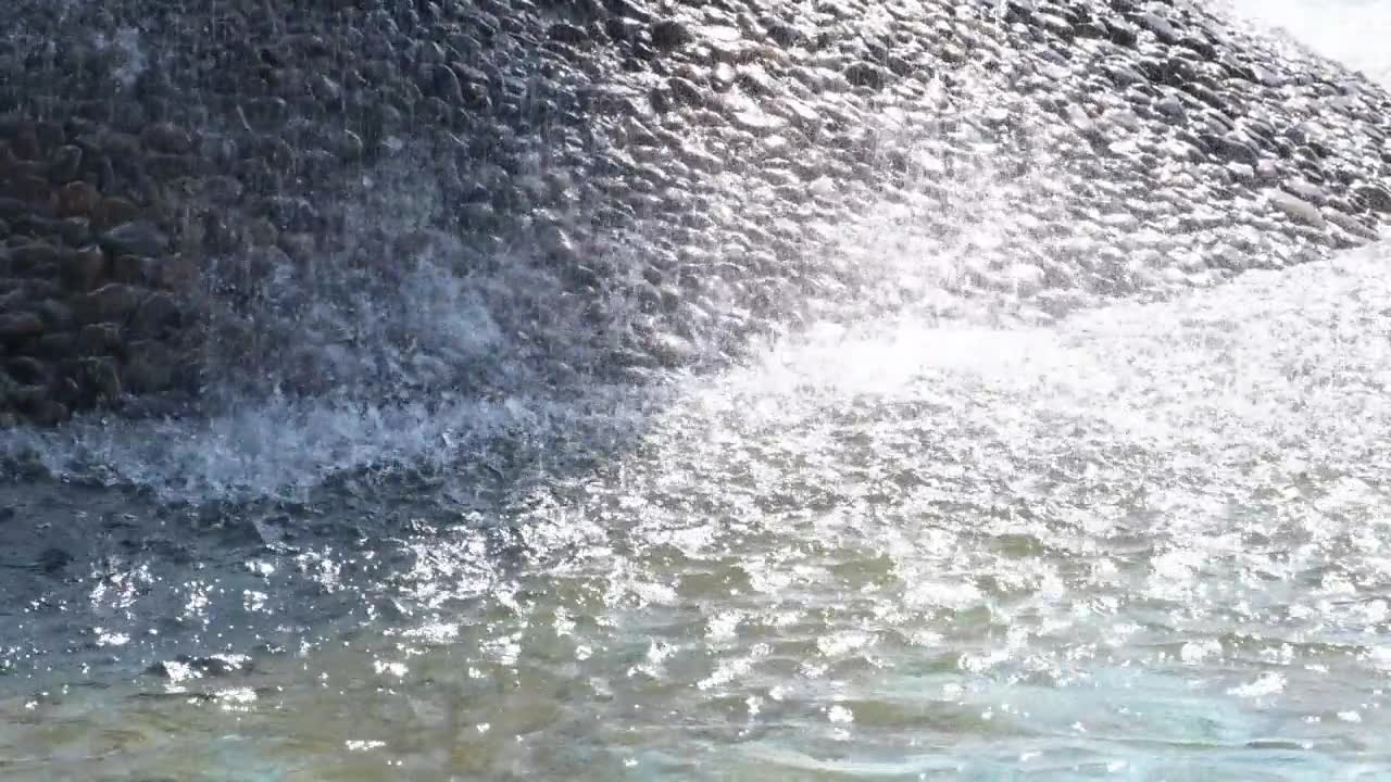 特写镜头：喷泉上的瀑布。水流如丝般光滑地流过装饰性的石坡。喷泉中的水闪烁发光，像液晶一样捕捉光线。视频素材画面1