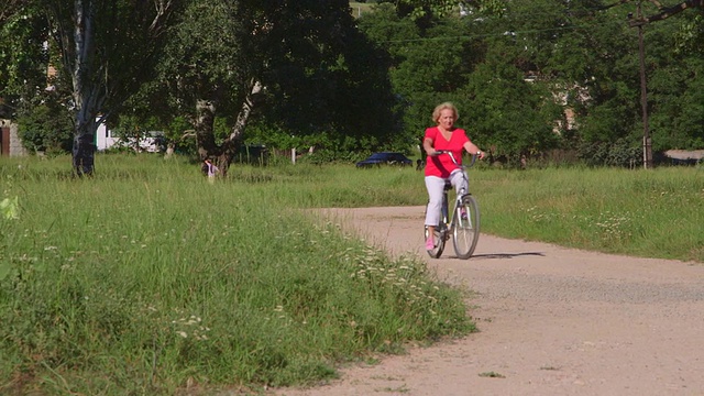 活跃的老年妇女沿着公园的道路骑自行车视频素材