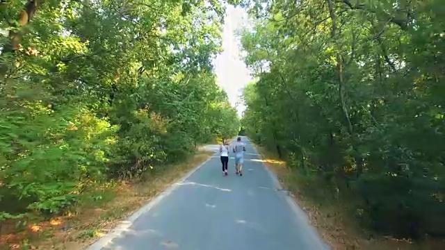 鸟瞰图的夫妇沿着森林的道路慢跑视频素材